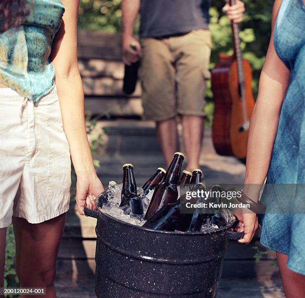 two women carrying bucket filled with beer and ice, mid section - balde imagens e fotografias de stock
