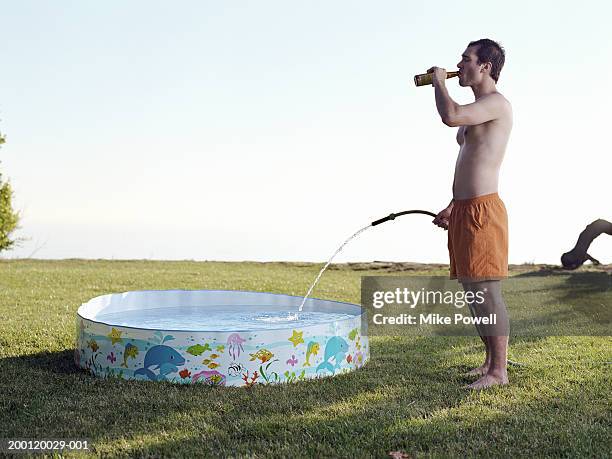 young man filling plastic pool with water from hose - plastic pool stockfoto's en -beelden
