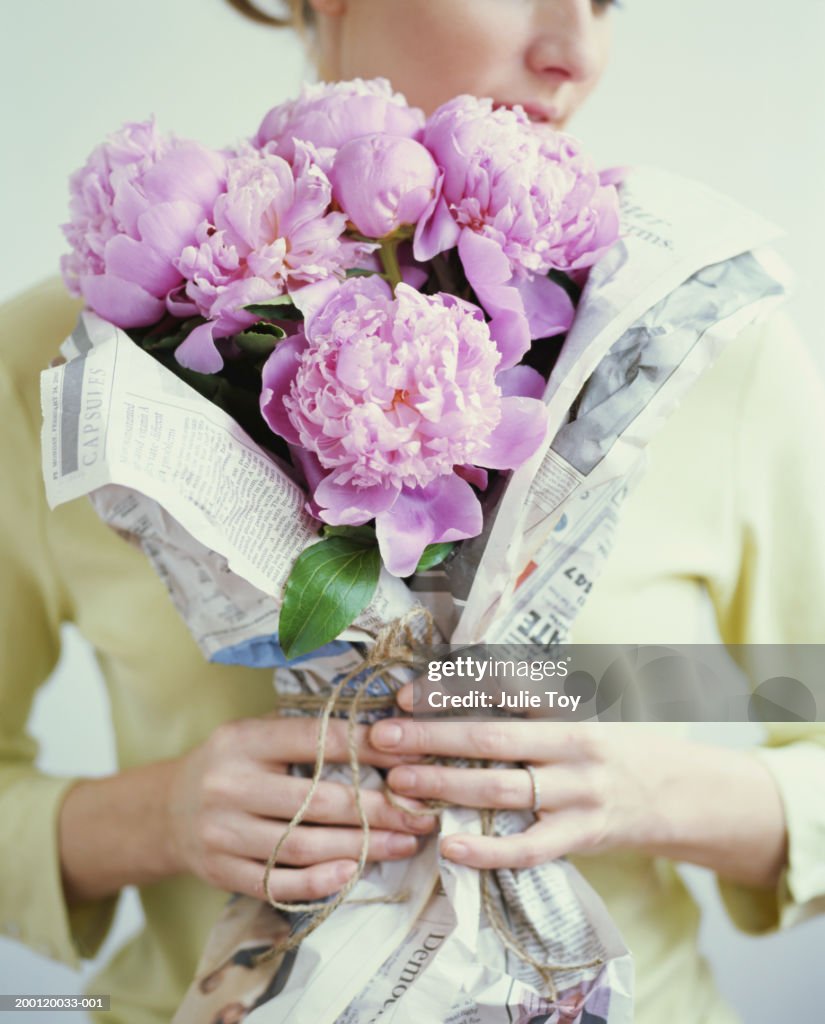 Woman holding bouquet of peonies wrapped in newspaper