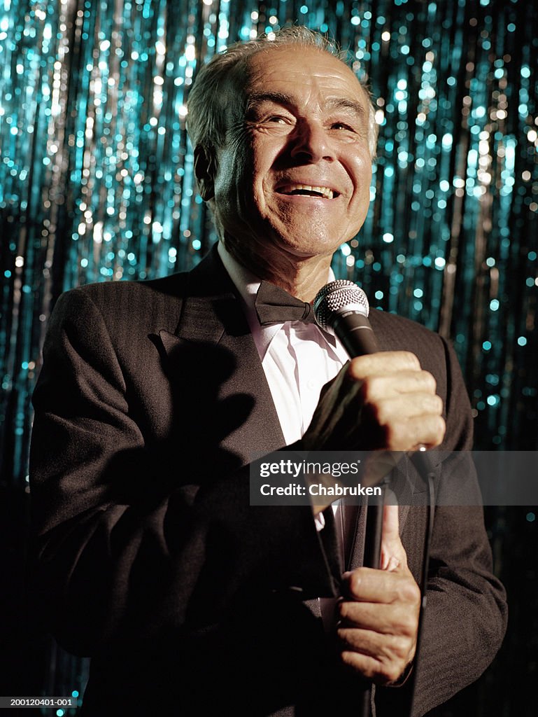 Mature man wearing tuxedo, standing on stage holding microphone