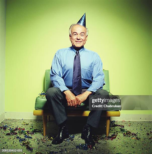 mature man in party hat sitting on sofa, confetti on floor - series finale party stockfoto's en -beelden