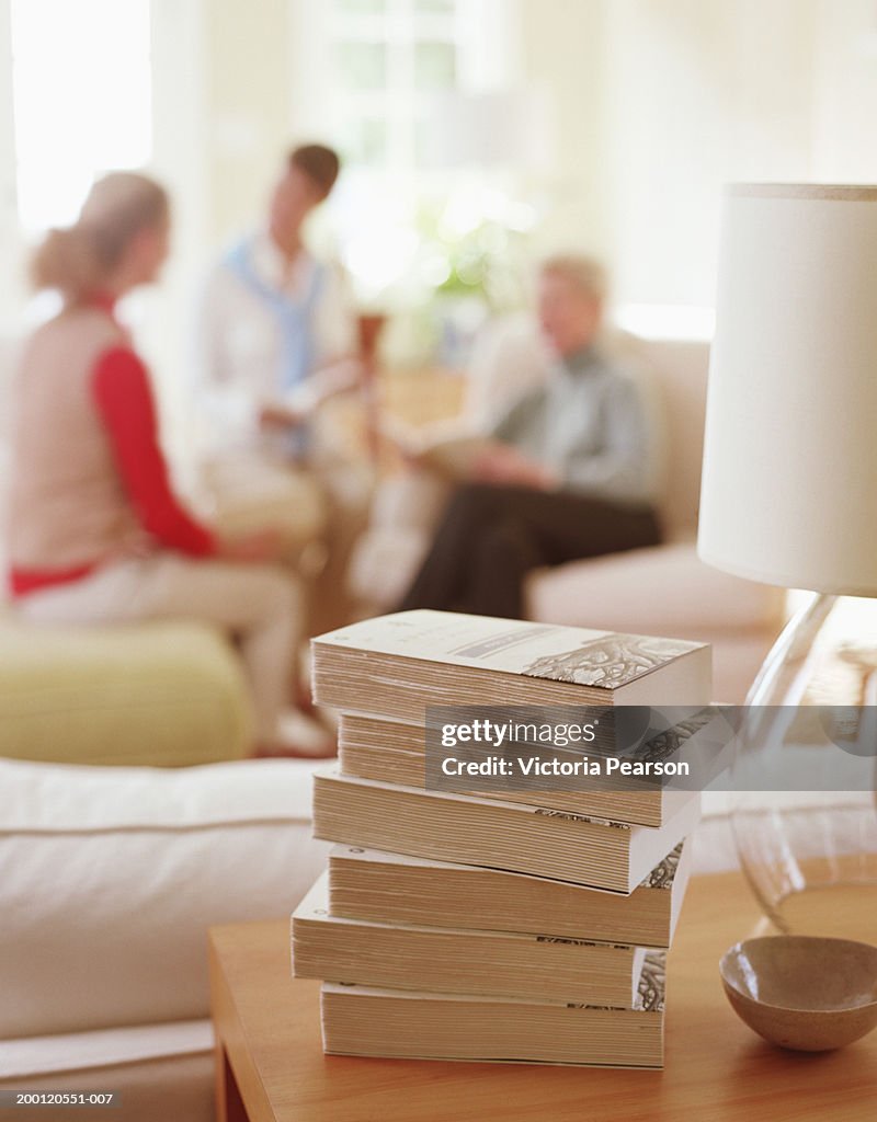 Stack of books sitting on table in living room, women in background