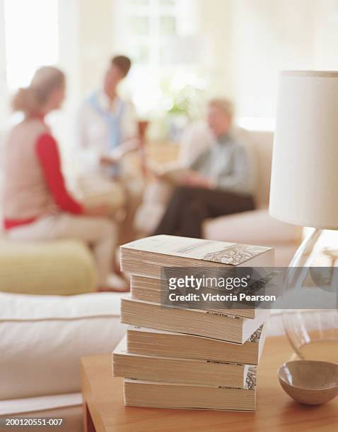 stack of books sitting on table in living room, women in background - paperback stock pictures, royalty-free photos & images