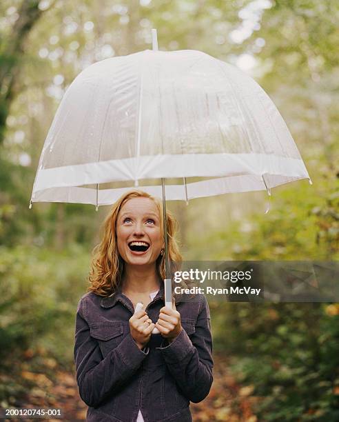 young woman standing under transparent umbrella, looking up - durchsichtig kleidung frau stock-fotos und bilder