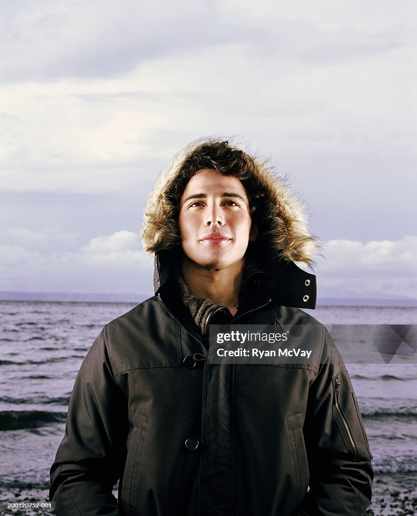 Young man standing beside sea, wearing hooded jacket, portrait