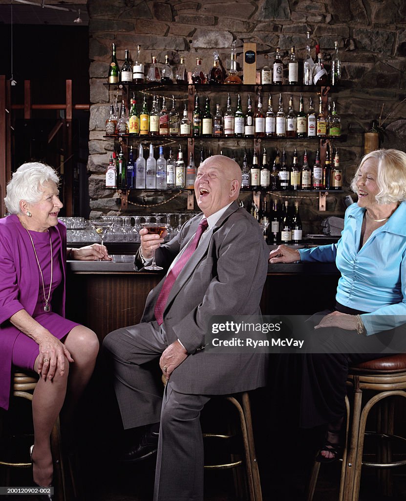 Three senior adults drinking martinis in bar, laughing