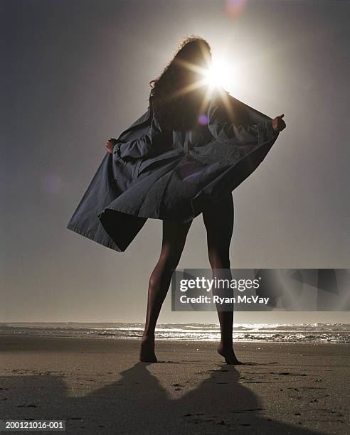 young woman holding trench coat open on beach, rear view - female flasher stock pictures, royalty-free photos & images