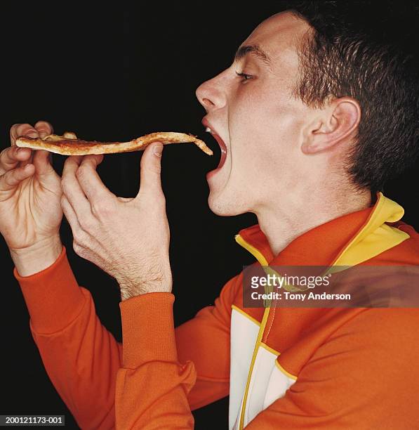 young man eating pizza, side view - pizza fotografías e imágenes de stock