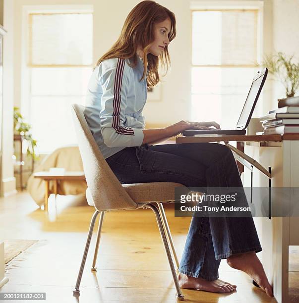 teenage girl (14-16) using laptop at home, side view - girls barefoot in jeans stockfoto's en -beelden