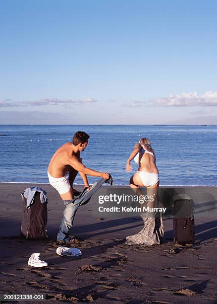 couple on beach stripping off clothes, rear view - couple swimwear stock pictures, royalty-free photos & images