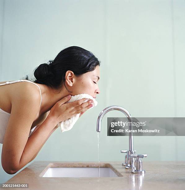 woman washing face with wash cloth over sink, side view - gesichtsreinigung stock-fotos und bilder