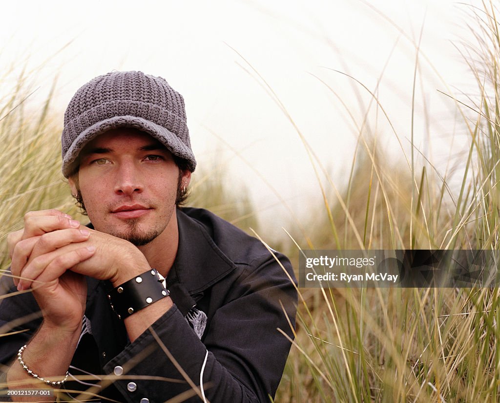 Young man surrounded by tall grass, hands clasped, portrait