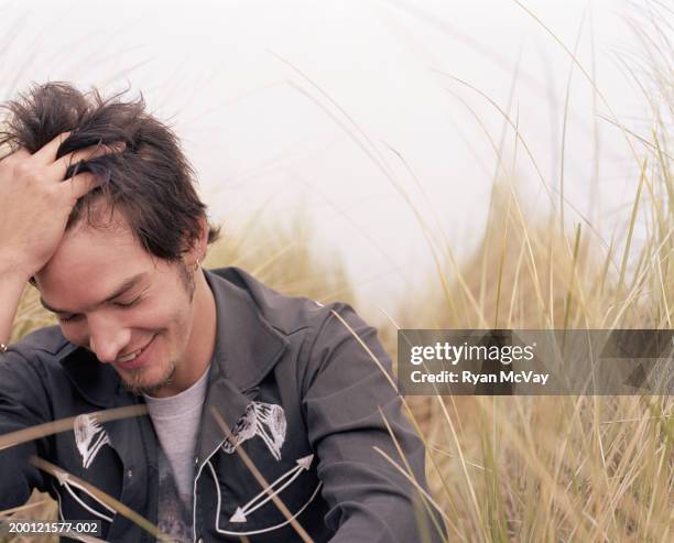 young man laughing, running fingers through hair - timido foto e immagini stock