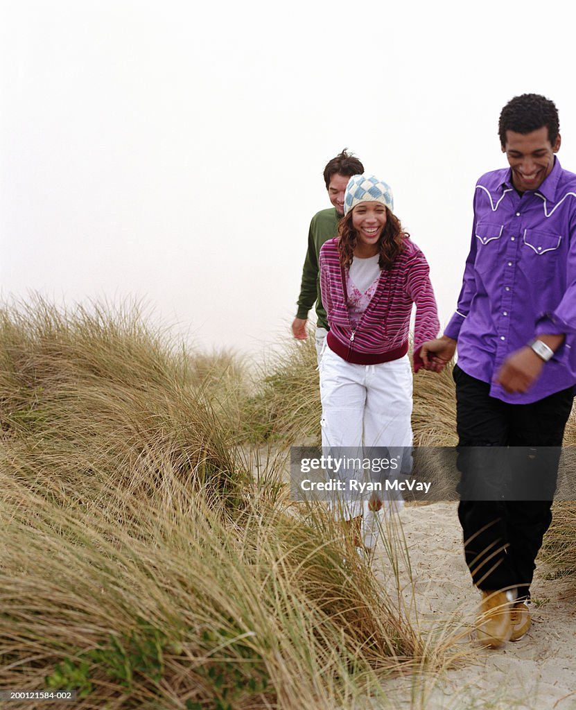 Three young adults running on sandy trail, laughing
