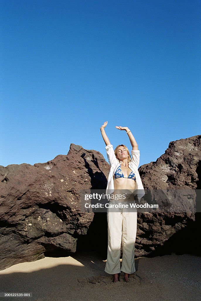 Woman stretching on beach, eyes closed