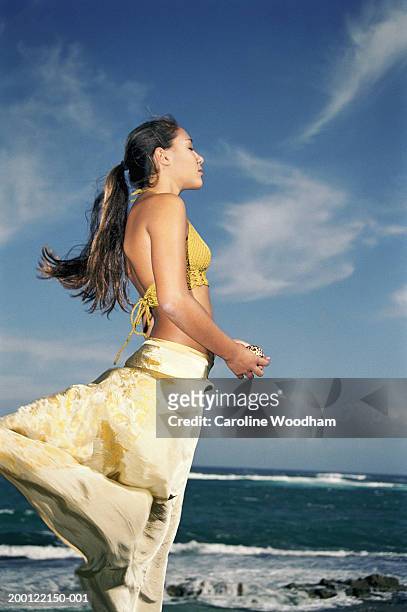 teenage girl (16-18) standing on beach, holding seashell, side view - windy skirt - fotografias e filmes do acervo
