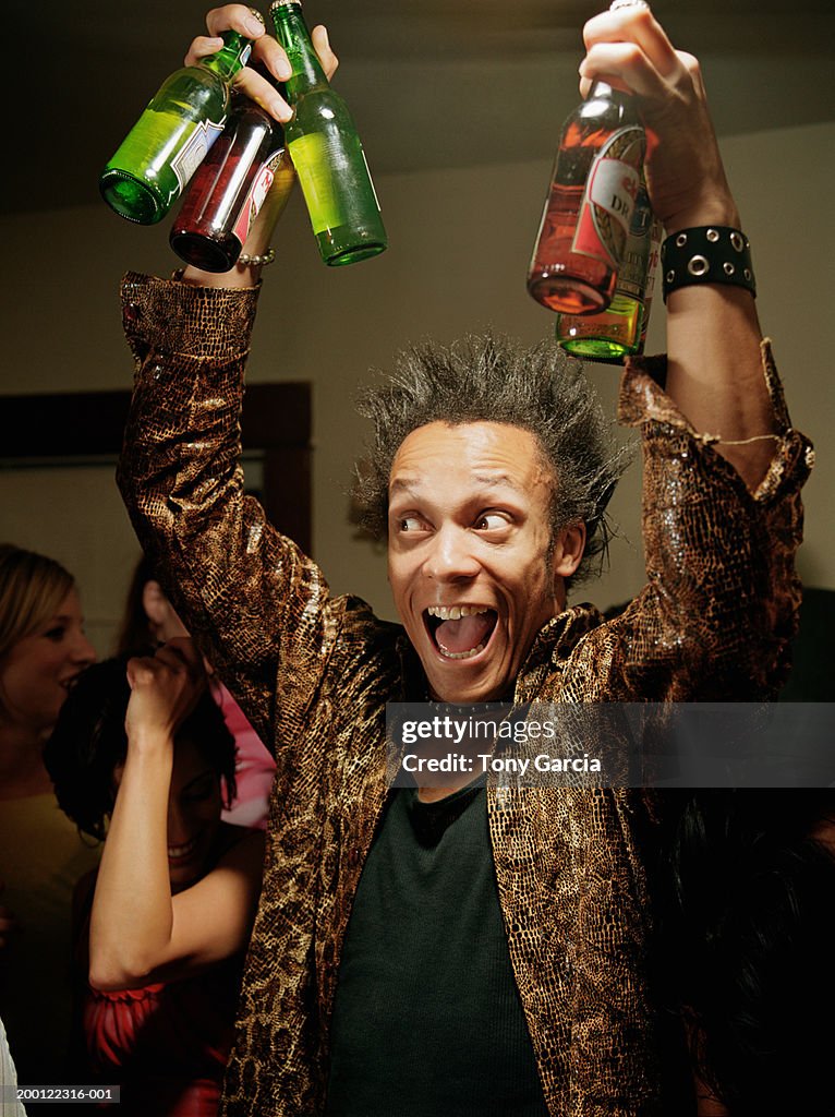 Young man holding up beer bottles at party