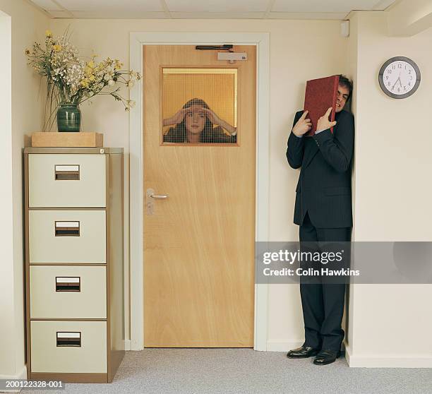 man in office hiding from woman peering through window in door - embuscade photos et images de collection