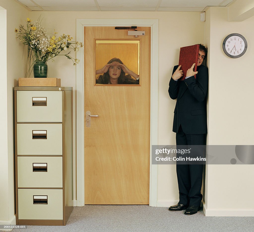Man in office hiding from woman peering through window in door