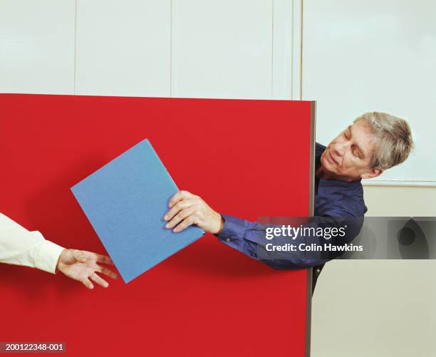 mature man passing file to colleague around partition - overdracht business mensen stockfoto's en -beelden