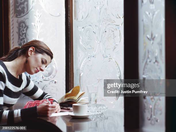 young woman writing postcard in pub - correspondence stockfoto's en -beelden