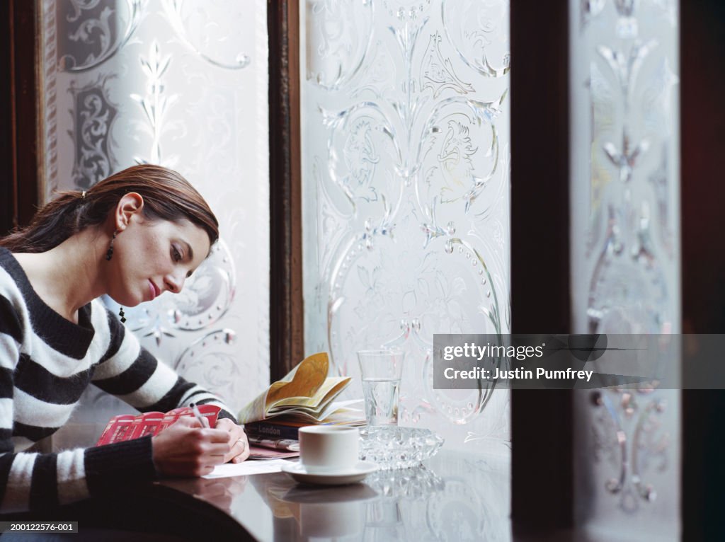 Young woman writing postcard in pub