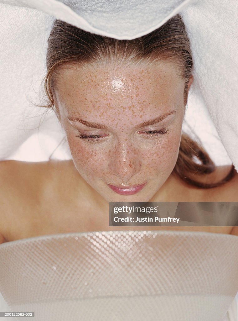 Young woman leaning over bowl, towel over head