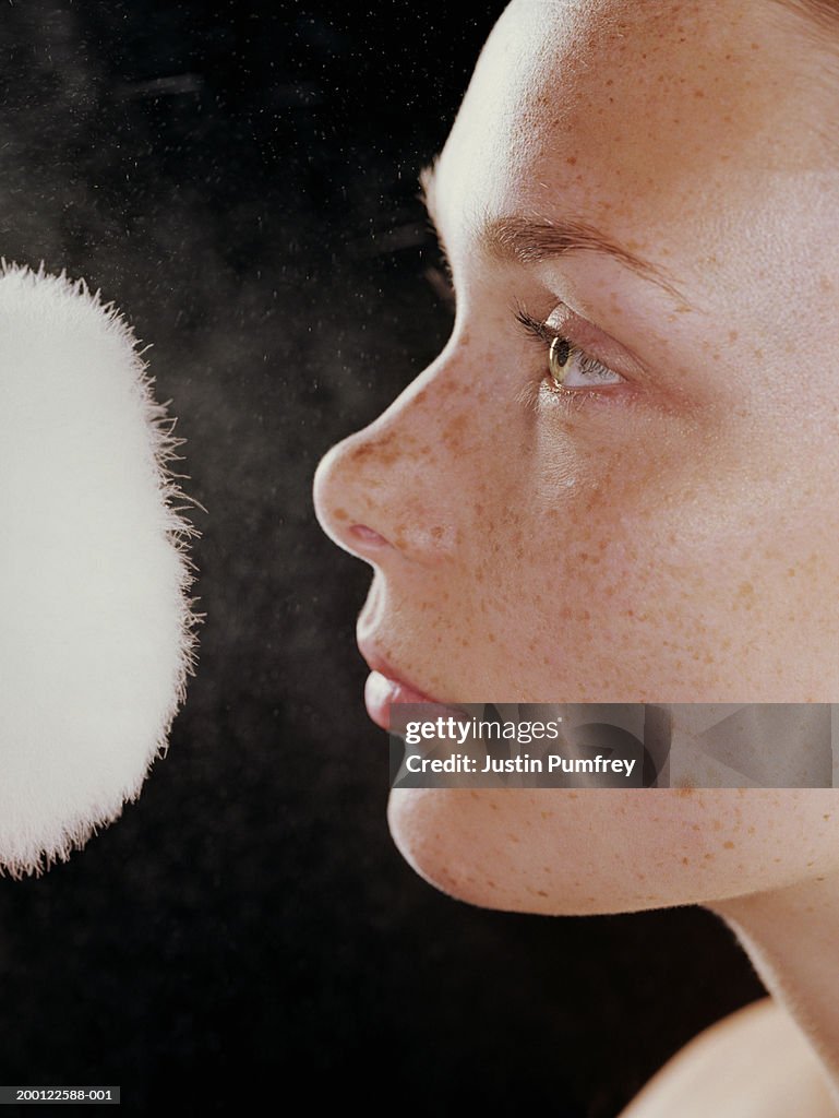 Young woman with powder puff in front of face, close-up, side view