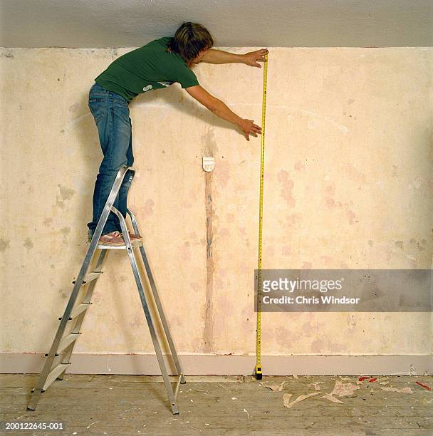 young man on stepladder holding tape measure against wall, side view - chris dangerous stock pictures, royalty-free photos & images