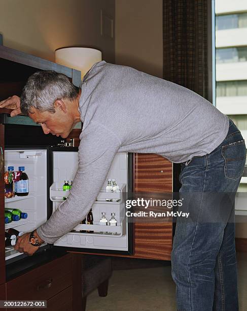 man looking in minibar in hotel room, side view - mini bar imagens e fotografias de stock