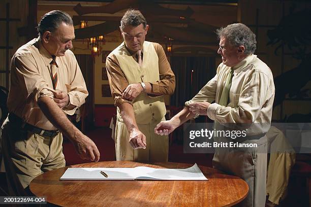 three men standing behind book on table, rolling up sleeves - roll shirt stock pictures, royalty-free photos & images