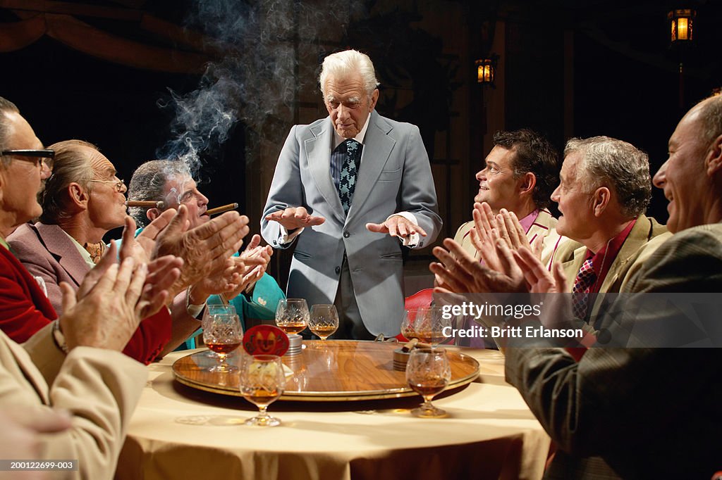 Mature businessmen at table, one standing gesturing with hands