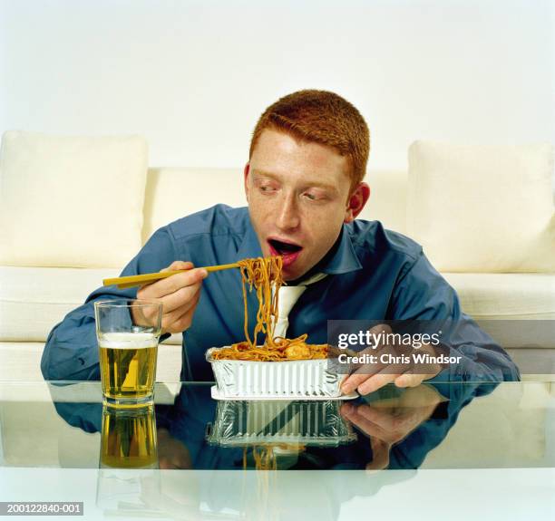 young man eating noodles from takeaway container - chinese takeout stock pictures, royalty-free photos & images