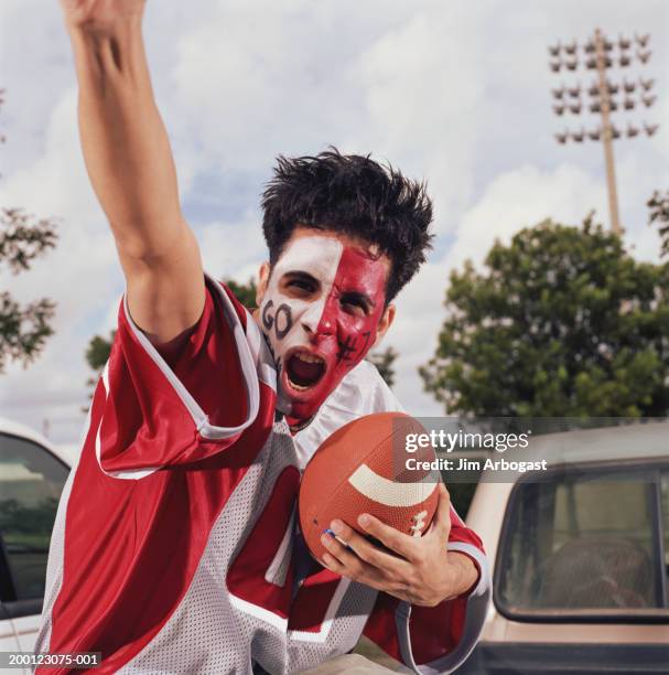 young man with painted face, cheering and holding football - american football fans stock pictures, royalty-free photos & images