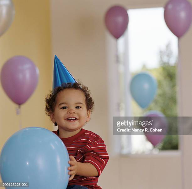 baby boy (12-15 months) holding balloon, wearing party hat, portrait - eerste verjaardag stockfoto's en -beelden