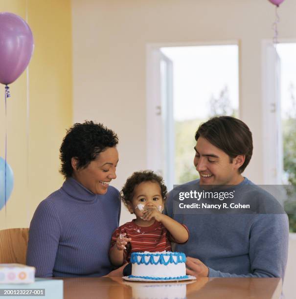 baby boy (12-15 months) sitting with parents, eating birthday cake - lampoon first birthday event stock-fotos und bilder