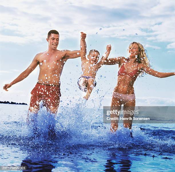 young couple swinging boy (2-4) over shallow water on beach - ankle deep in water - fotografias e filmes do acervo