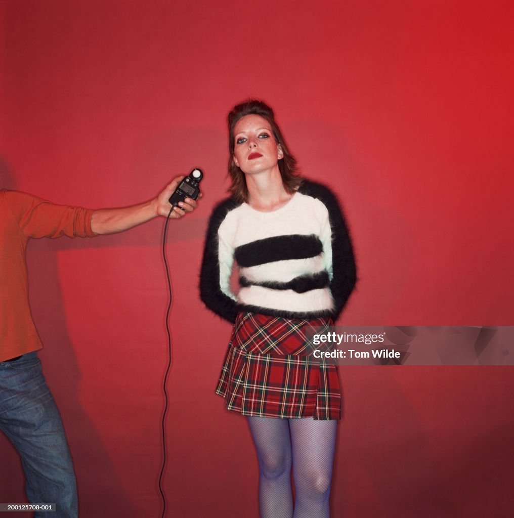 Model against red background, photographer using light meter