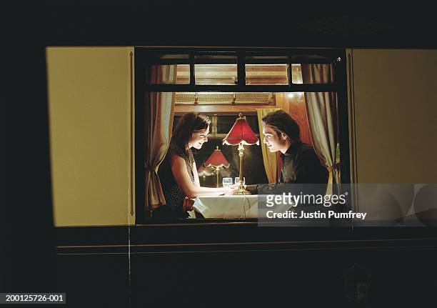 young couple at table aboard train, exterior view, night - cortejar fotografías e imágenes de stock