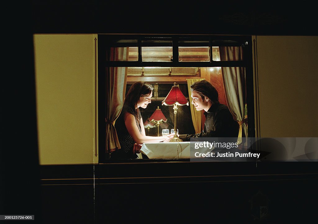 Young couple at table aboard train, exterior view, night