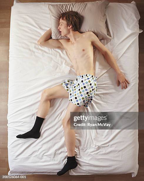 young man sleeping on top of sheets in boxers and socks, overhead view - above view of man sleeping on bed stock-fotos und bilder