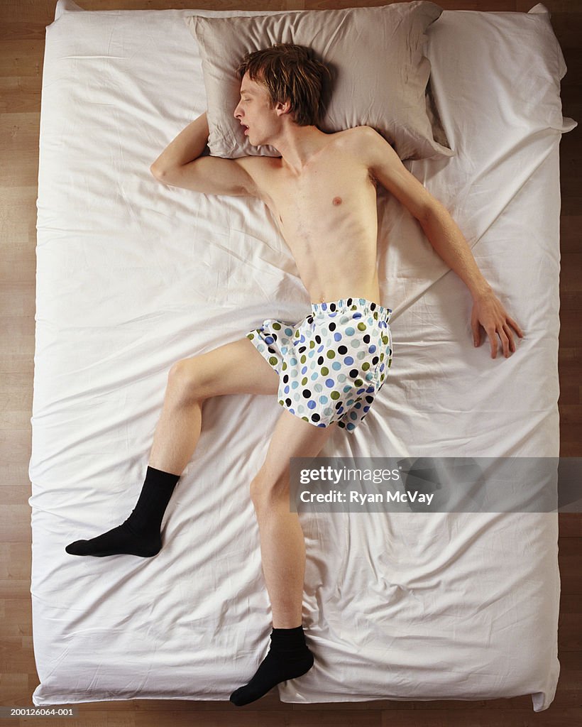Young man sleeping on top of sheets in boxers and socks, overhead view