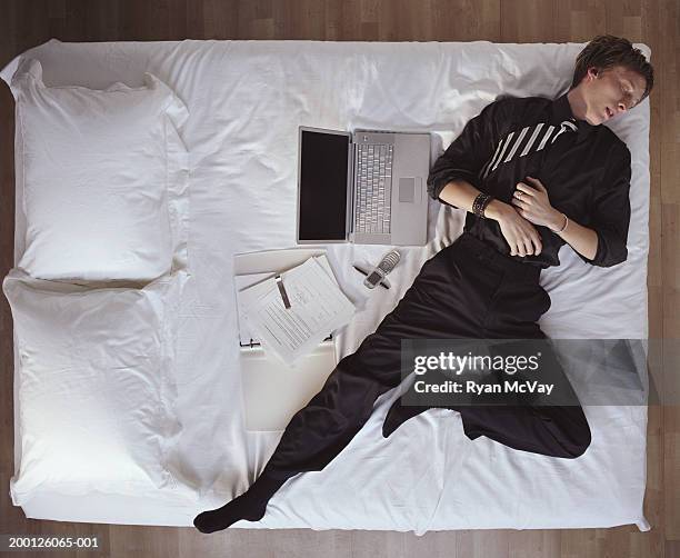 young man in suit, sleeping on bed next to laptop, overhead view - above view of man sleeping on bed stock pictures, royalty-free photos & images