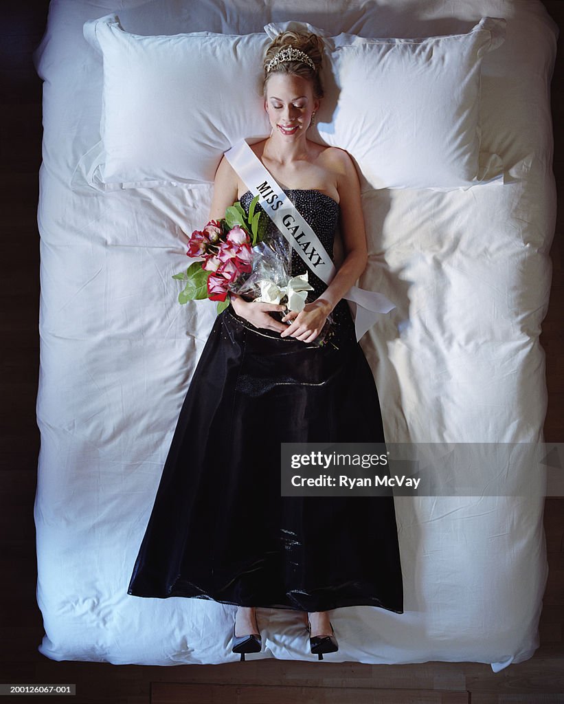 Young beauty queen lying on bed in full dress, overhead view