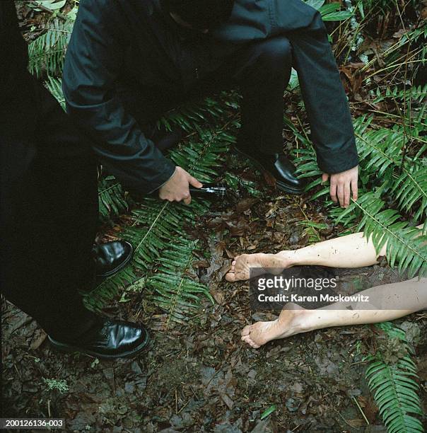 two men investigating dead body lying in woods, elevated view - dead women stockfoto's en -beelden