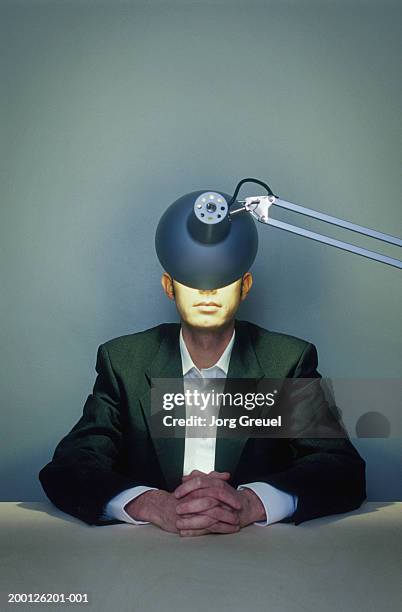 businessman with hands clasped, illuminated lamp obscuring face - interrogatorio foto e immagini stock