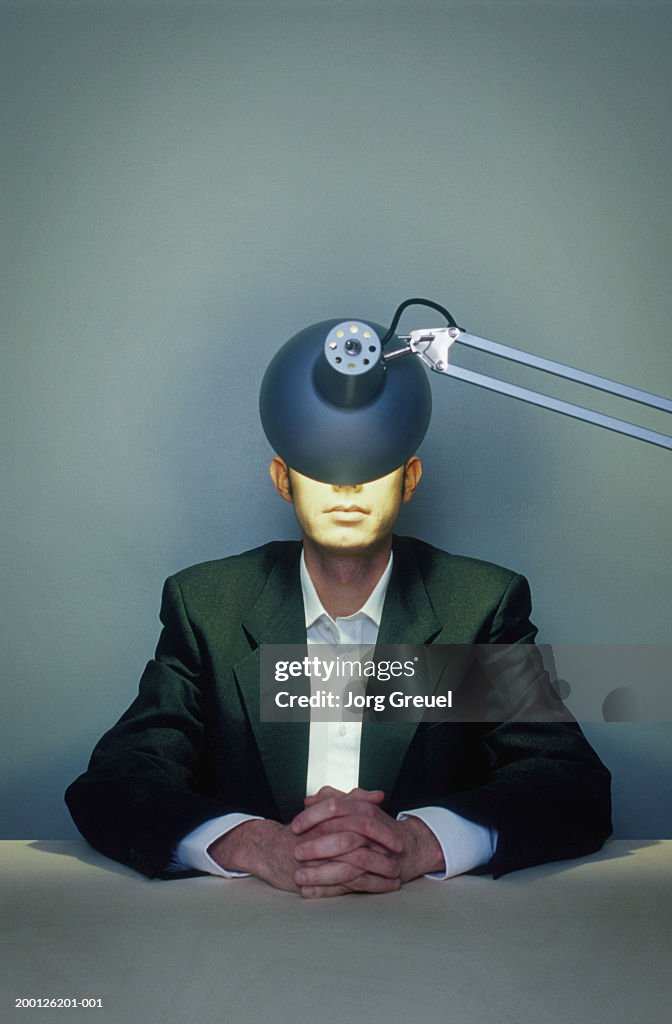 Businessman with hands clasped, illuminated lamp obscuring face