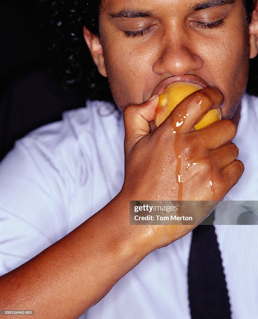 Businessman biting peach, juice running down hand, close-up