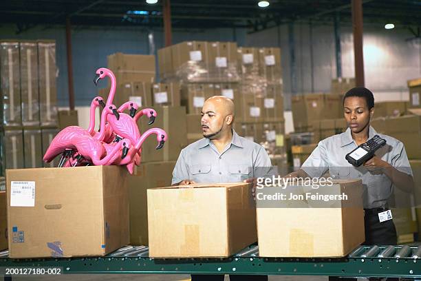 man looking at plastic flamingos on conveyor belt, woman scanning box - flamingos stock-fotos und bilder