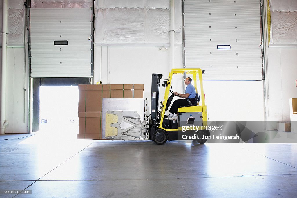 Man driving squeeze with boxes through warehouse, side view